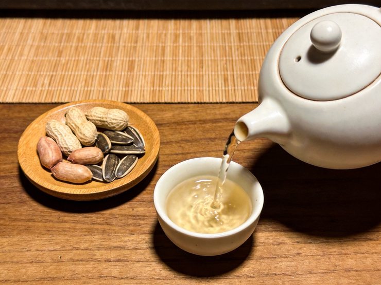 白瓷茶壶往小茶杯里倒茶,旁边放着几粒花生和瓜子